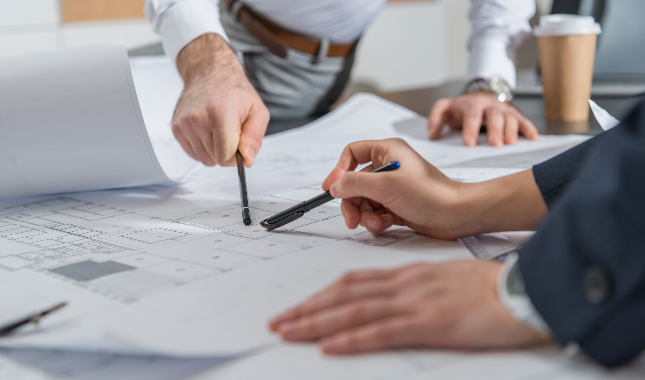 Architekten besprechen Baupläne am Tisch mit Zeichnungen, Stiften und Kaffeebecher in professioneller Umgebung