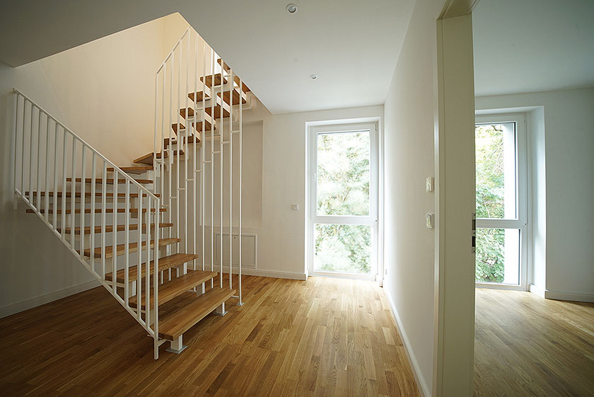 Moderner Flur mit Holztreppe, großen Fenstern und Parkettboden in einem hellen, lichtdurchfluteten Wohnbereich