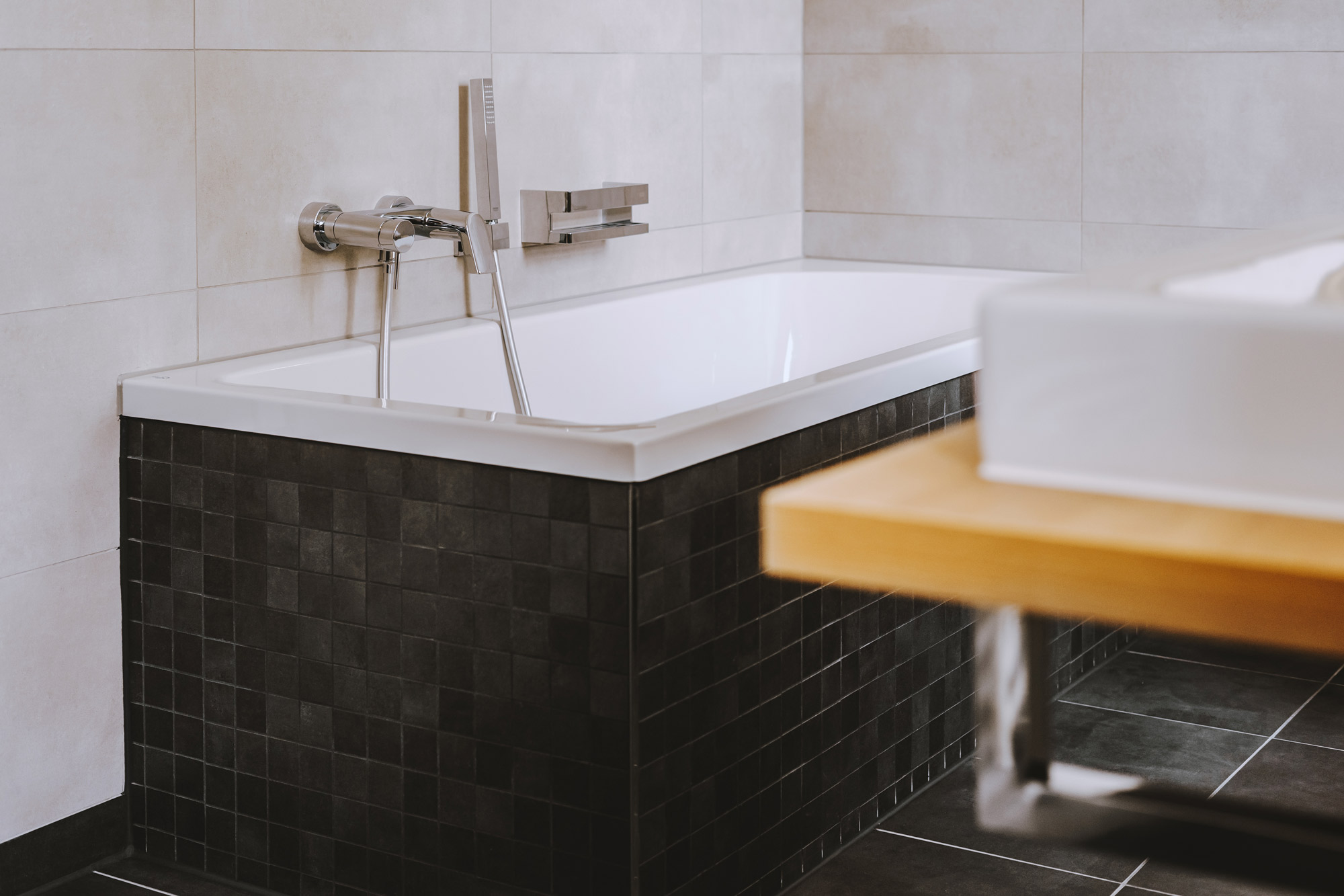 Modernes Badezimmer mit eingebauter Badewanne, dunkler Verkleidung, Wandfliesen und Waschtisch mit Holzplatte