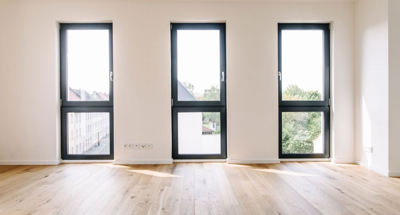 Heller Raum mit drei bodentiefen Fenstern, Eichenparkett und weiß gestrichenen Wänden in moderner Stadtwohnung
