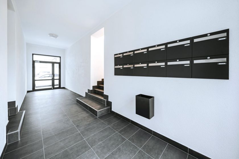 Moderner Hauseingang mit schwarzen Briefkästen, grauen Bodenfliesen und Glastür in einem Mehrfamilienhaus