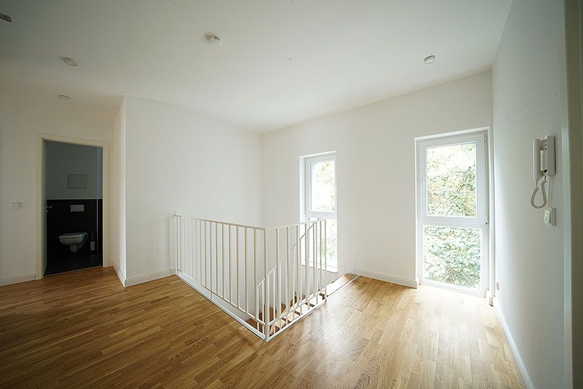 Heller Flur mit Holzfußboden, Treppenabgang, großen Fenstern und Zugang zu einem modernen Badezimmer