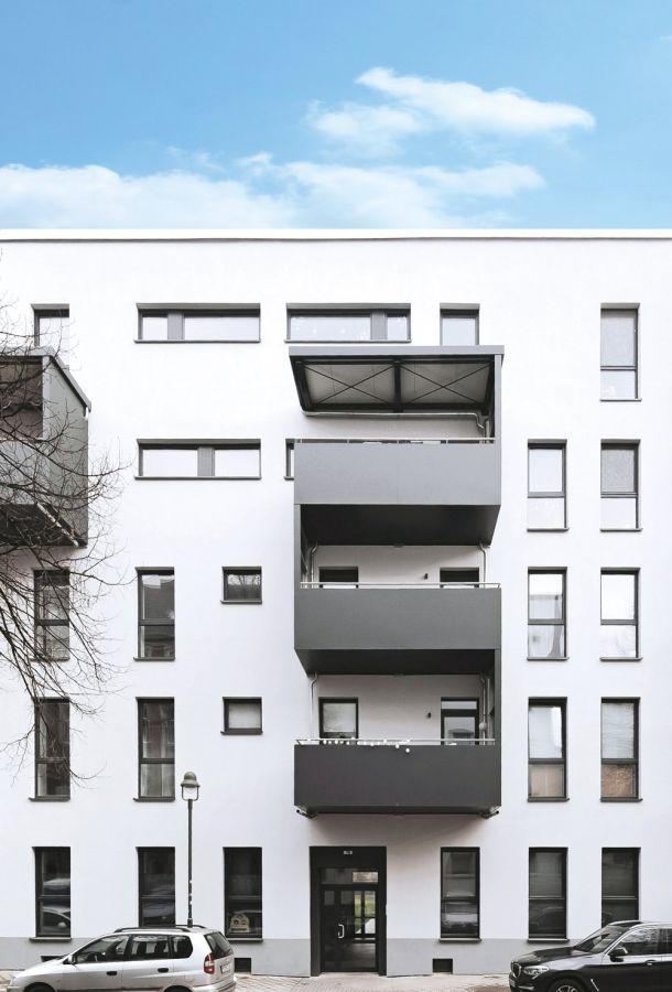 Modernes Mehrfamilienhaus mit weißen Fassaden, grauen Balkonen und geparkten Autos in urbaner Umgebung bei Tag