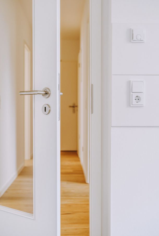 Geöffnete weiße Innentür mit Edelstahlgriff in modernem Flur mit Parkettboden und weißen Wänden