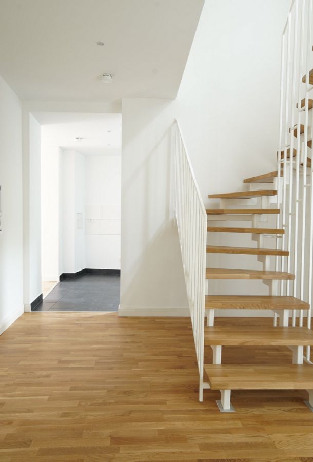 Heller Eingangsbereich mit moderner Holztreppe, Eichenparkett und weiß gestrichenen Wänden in einer Neubauwohnung