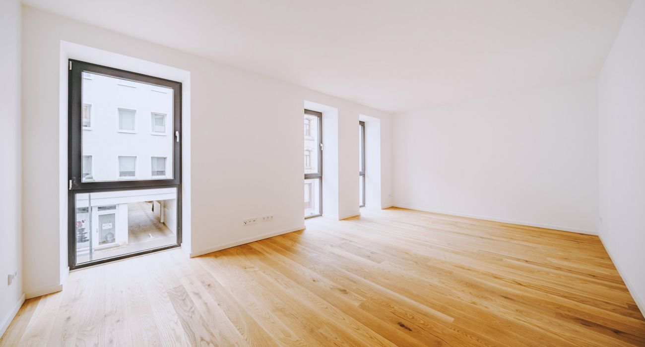 Helles, leeres Zimmer mit großen Fenstern, Eichenparkett und weißen Wänden in einem modernen Neubau