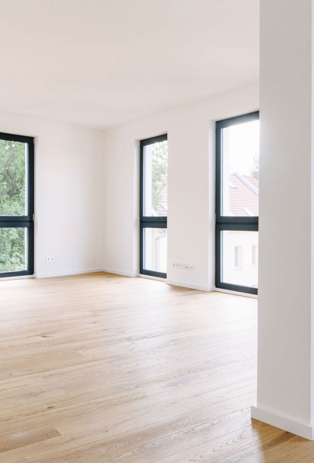 Helles, modernes Wohnzimmer mit großen Fenstern, Eichenparkett und weiß gestrichenen Wänden in einer Neubauwohnung