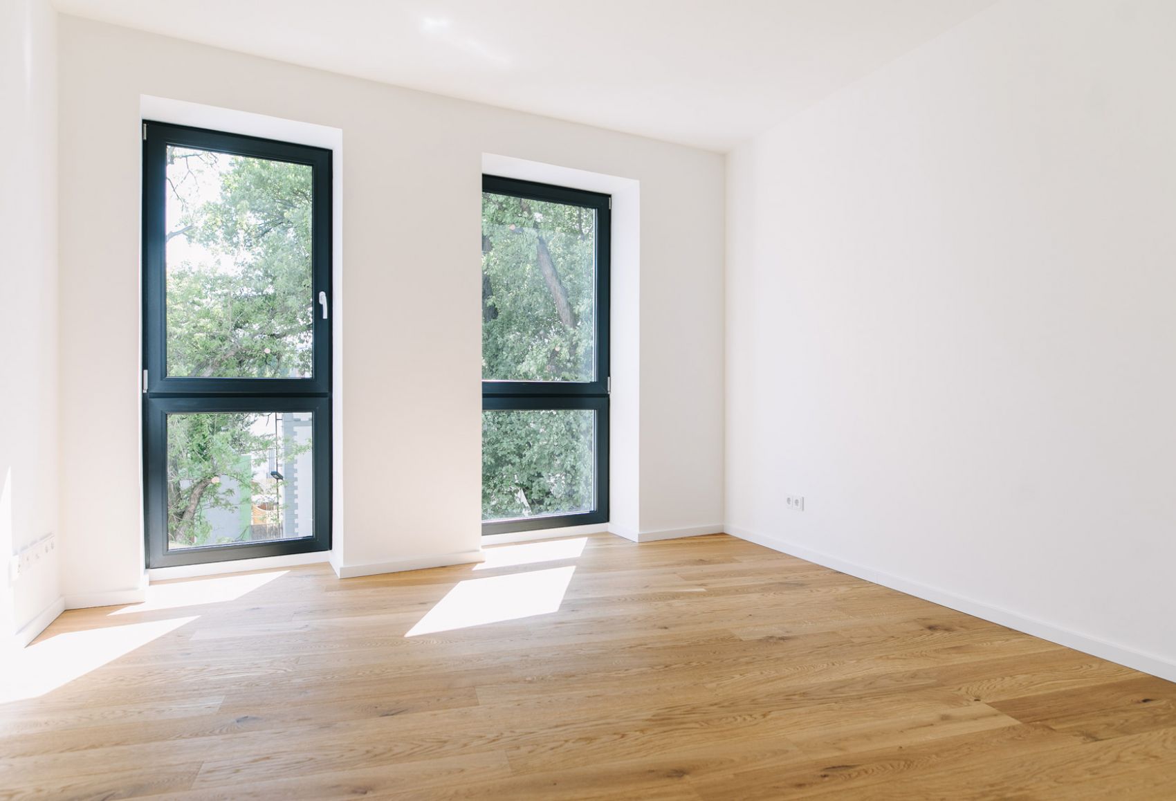 Helles Zimmer mit großen Fenstern, Eichenparkett und weißer Wandgestaltung in moderner Wohnimmobilie