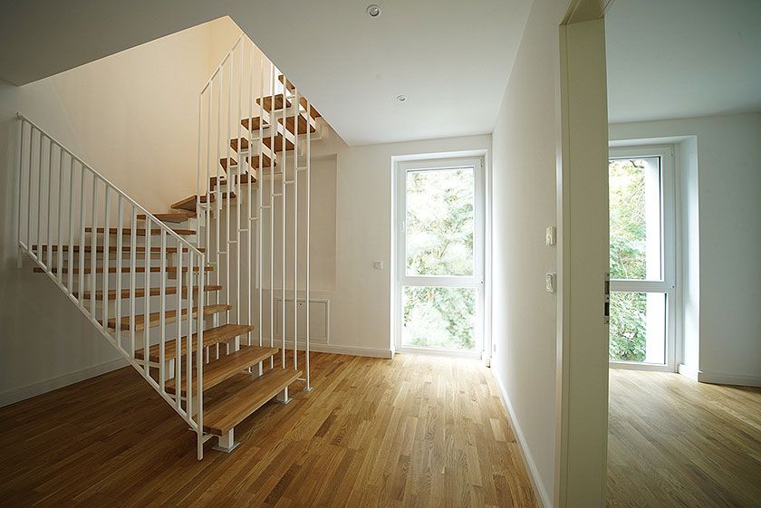 Moderner Flur mit Holztreppe, großen Fenstern und Parkettboden in einem hellen, lichtdurchfluteten Wohnbereich