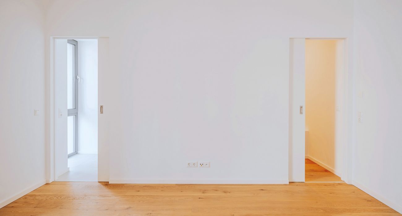 Minimalistischer Raum mit zwei Schiebetüren, Eichenparkett und weiß gestrichenen Wänden in moderner Neubauwohnung