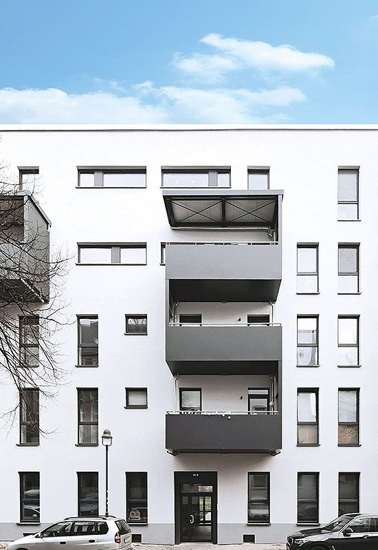 Modernes Mehrfamilienhaus mit weißen Fassaden, grauen Balkonen und geparkten Autos in urbaner Umgebung bei Tag