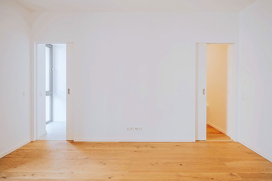 Minimalistischer Raum mit zwei Schiebetüren, Eichenparkett und weiß gestrichenen Wänden in moderner Neubauwohnung