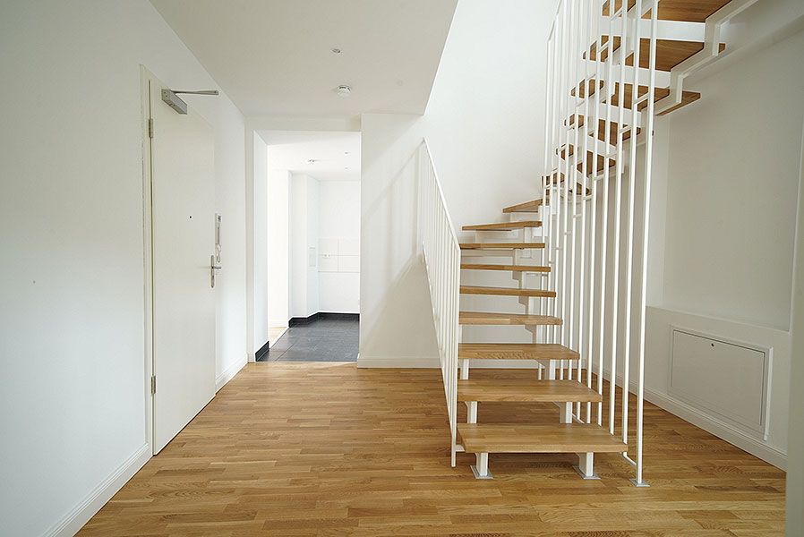 Heller Eingangsbereich mit moderner Holztreppe, Eichenparkett und weiß gestrichenen Wänden in Neubauwohnung