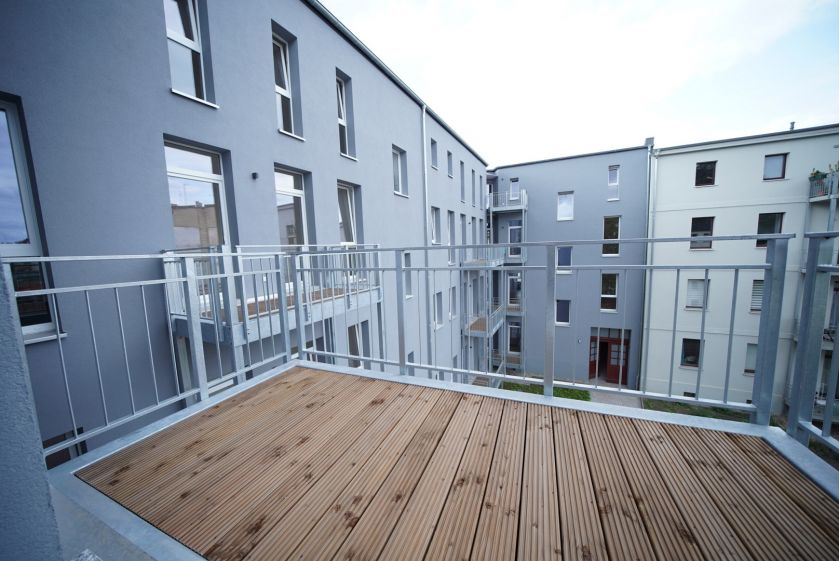 Innenhofansicht moderner Mehrfamilienhäuser mit Balkonen, grauer Fassade und Terrasse mit Holzbelag und Metallgeländer