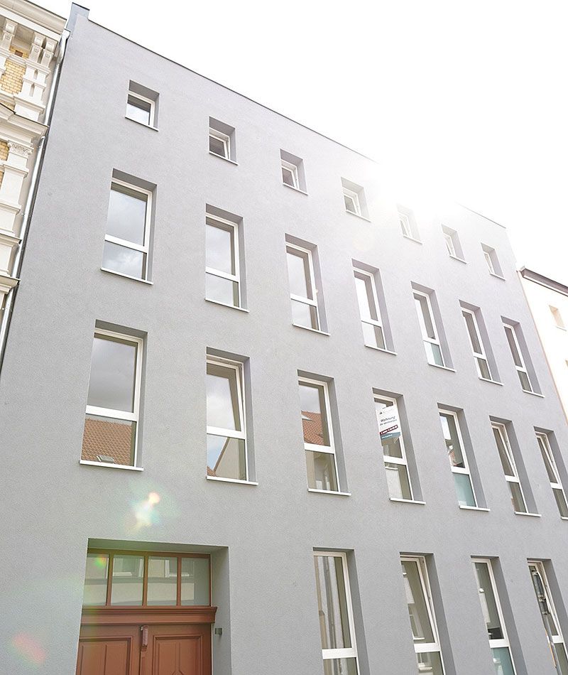 Moderne graue Hausfassade mit symmetrisch angeordneten Fenstern und Holzeingangstür im Sonnenschein