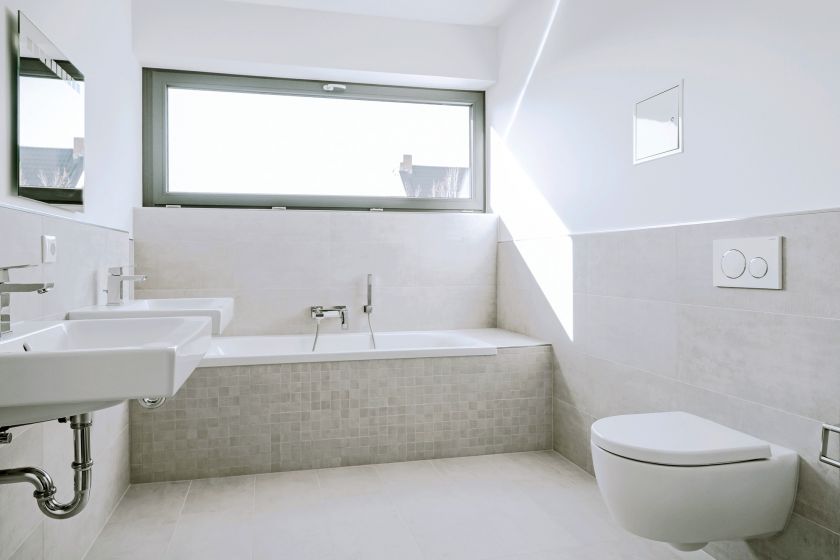 Modernes Badezimmer mit Badewanne, zwei Waschbecken, Hänge-WC und großem Fenster, gestaltet in hellen Naturtönen