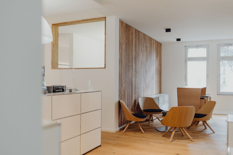 Modern eingerichteter Wartebereich mit Holzstühlen, Holzboden und Wandverkleidung in einem hellen Büro oder Empfangsraum