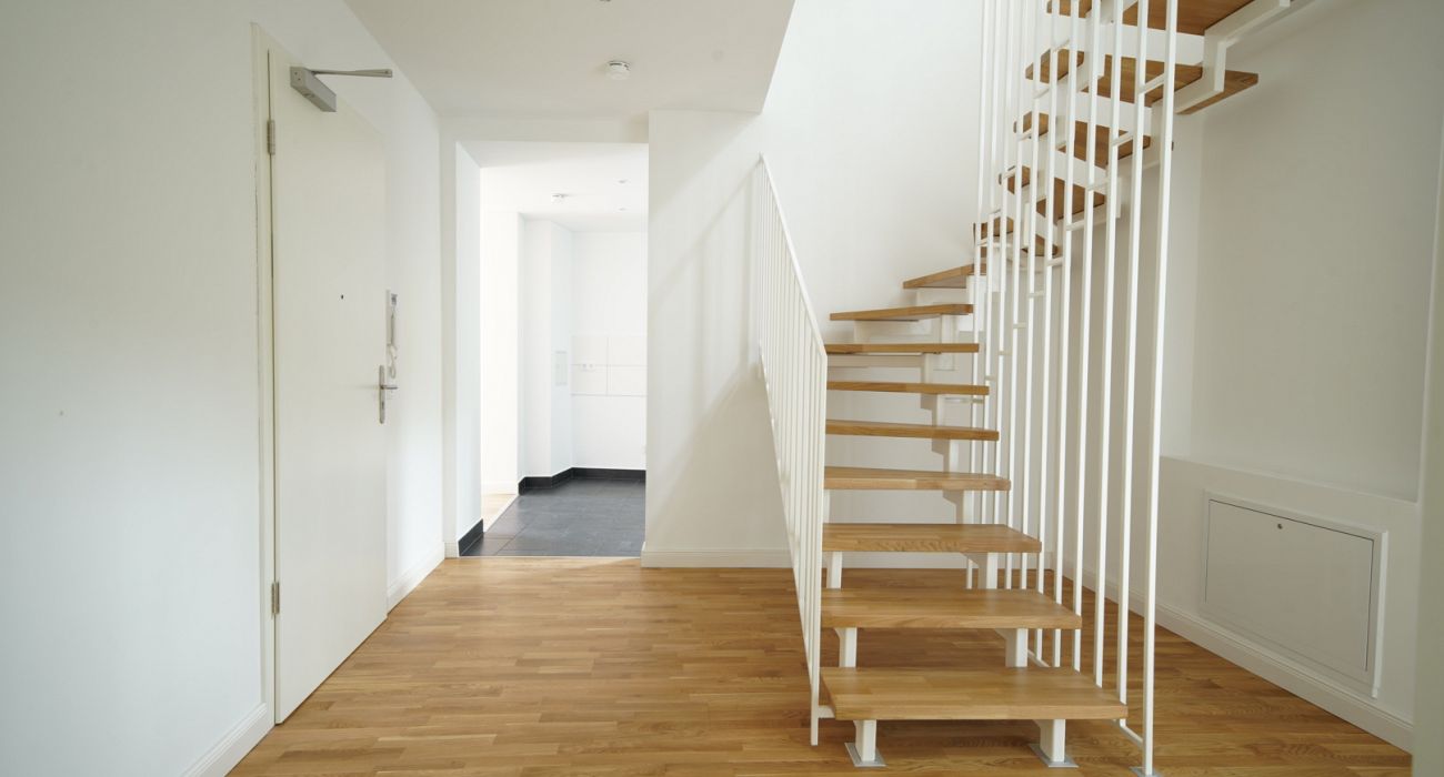 Heller Eingangsbereich mit moderner Holztreppe, Eichenparkett und weiß gestrichenen Wänden in einer Neubauwohnung