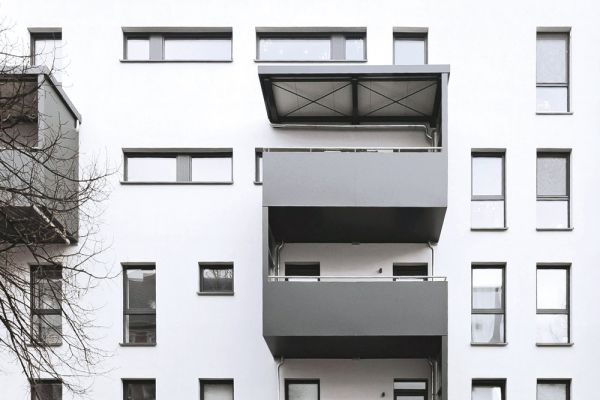 Modernes Mehrfamilienhaus mit weißen Fassaden, grauen Balkonen und geparkten Autos in urbaner Umgebung bei Tag