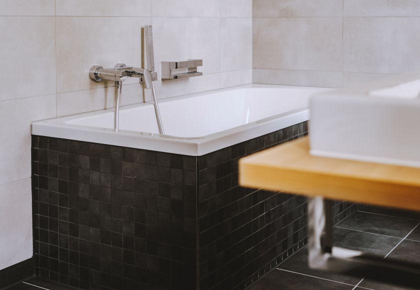 Moderne Badewanne mit schwarzer Fliesenverkleidung und Wandarmatur in stilvollem Badezimmer mit hellen Wandfliesen
